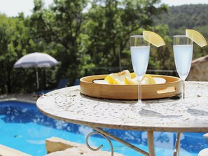 A poolside table with two glasses of a clear beverage, a wooden tray with sliced fruit, and a pool in the background. - Holiday house for 6 guests with private pool (Aigues-Vives)