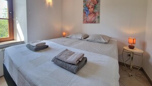 Een slaapkamer met twee bedden, een raam en een schilderij aan de muur.
