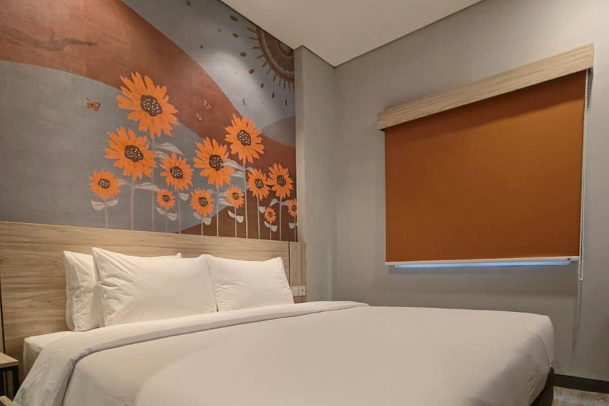 Une chambre à coucher avec un grand lit, une tête de lit en bois, une table de chevet et une fresque murale représentant des tournesols.