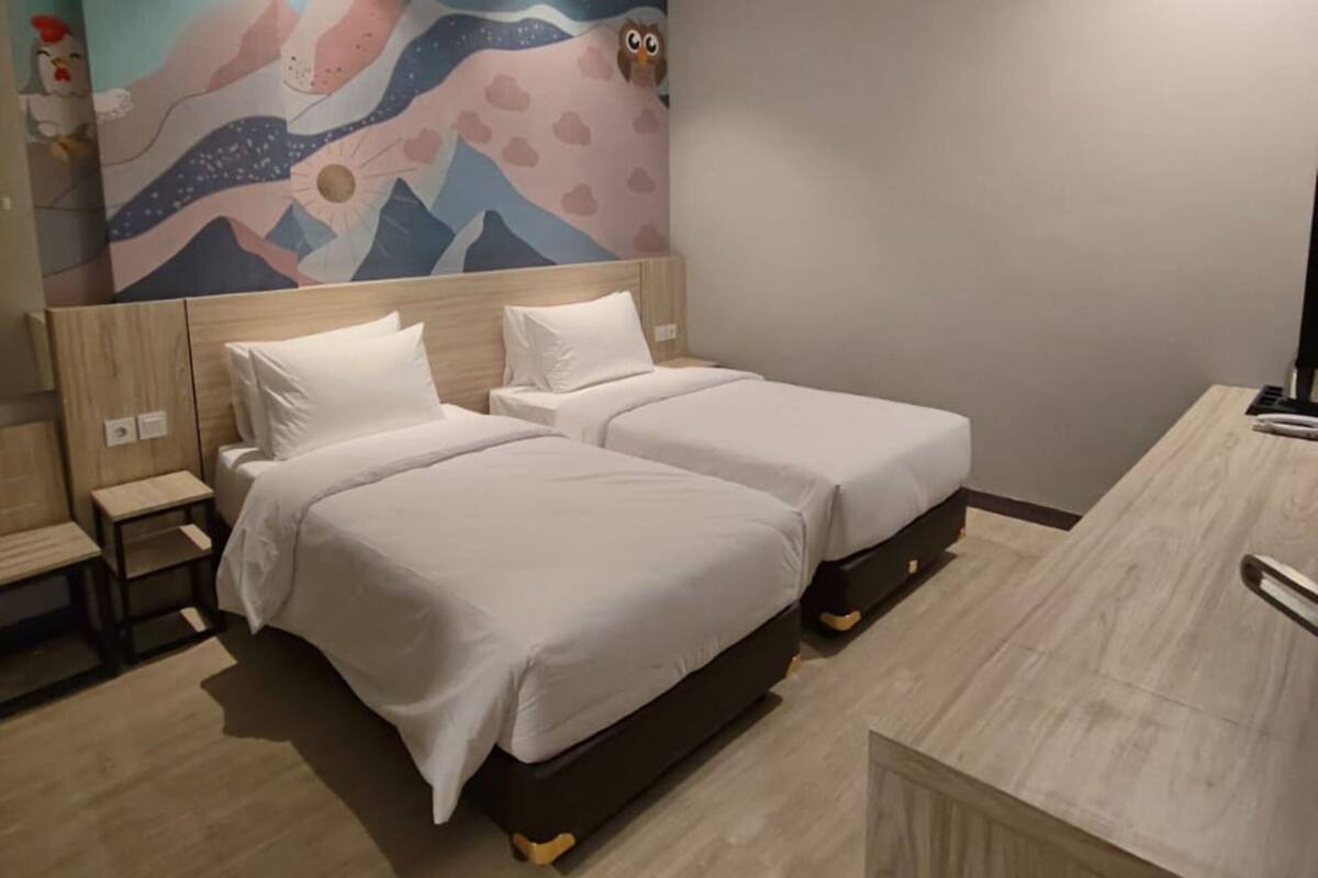 Une chambre d’hôtel avec deux lits, une table de chevet, un bureau et une fresque murale.