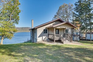 A single-story cabin with a porch, located near a lake with trees and hills in the background. - Dock & Views: Waterfront Home in Wabasha! (Wabasha)
