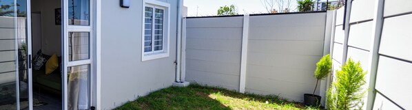 Une façade extérieure d’habitation avec un mur extérieur blanc, une petite pelouse et un pot de fleurs.