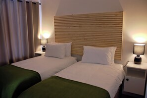 Une chambre d’hôtel avec deux lits simples, une tête de lit en bois, des lampes de chevet et un plaid vert.