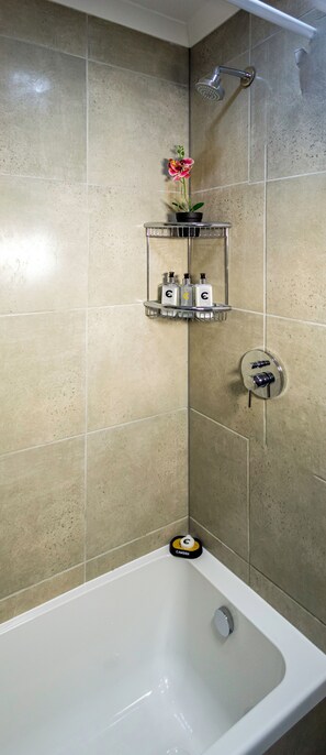 Une salle de bain équipée d’une baignoire, d’une douche et de deux étagères en métal où sont rangés les articles de toilette.