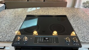 Une cuisine avec une plaque de cuisson noire, des comptoirs en granit et un canapé en cuir marron à l’arrière-plan.