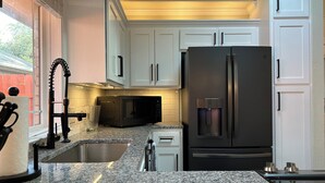 Une cuisine moderne avec des meubles blancs, un réfrigérateur noir, un four à micro-ondes et un évier en acier inoxydable.