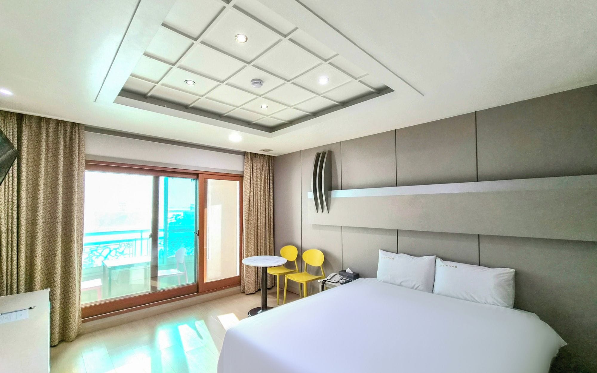 A hotel room with a large bed, a desk, a chair, a small table, and a view of the outside.