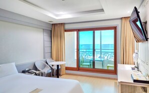 A hotel room with a bed, a desk, a chair, a small table, a TV, and a balcony with a view of the sea. - Bon Gaya Hotel (Boryeong)