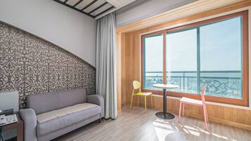Habitación moderna con sofá, una mesita, una silla y un gran ventanal con vista al mar.