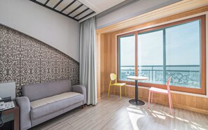 A modern room with a sofa, a small table, a chair, and a large window offering a view of the sea. - Bon Gaya Hotel (Boryeong)