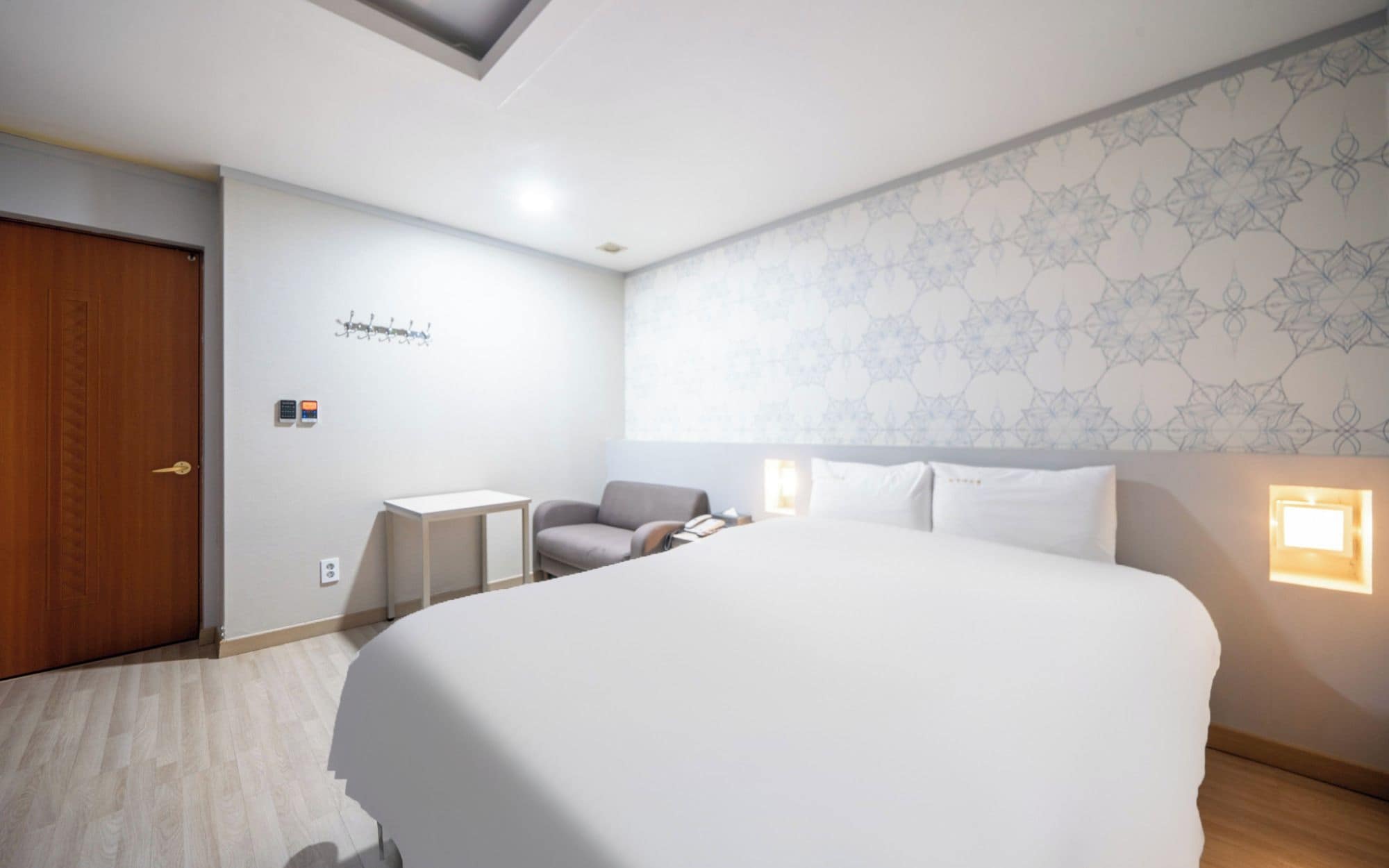 Habitació d'hotel amb un llit gran, una taula de treball, una cadira, una perxa per a abrics i un mur amb dibuixos.
