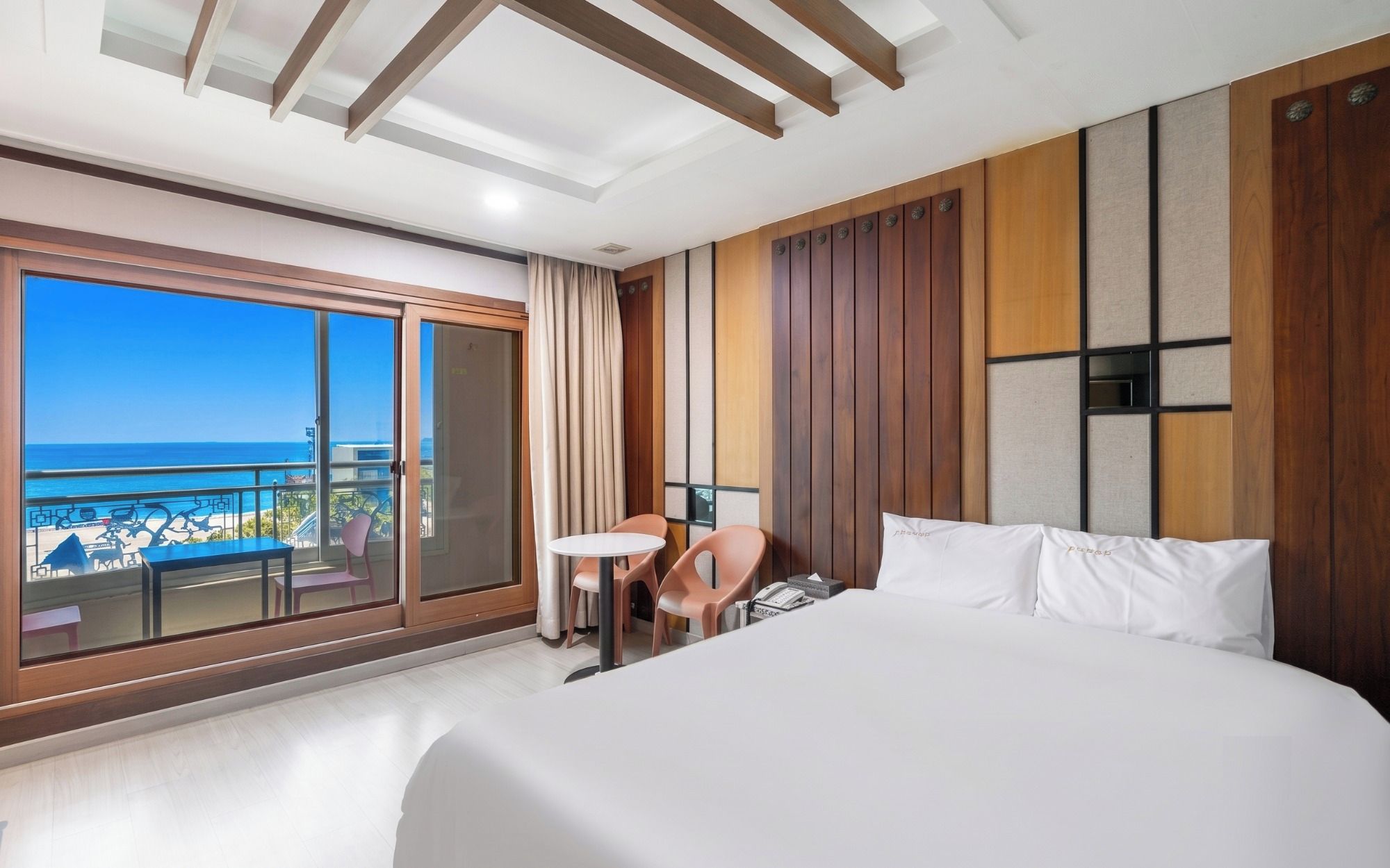 A hotel room with a large bed, a small table, a chair, a phone, and a view of the ocean.