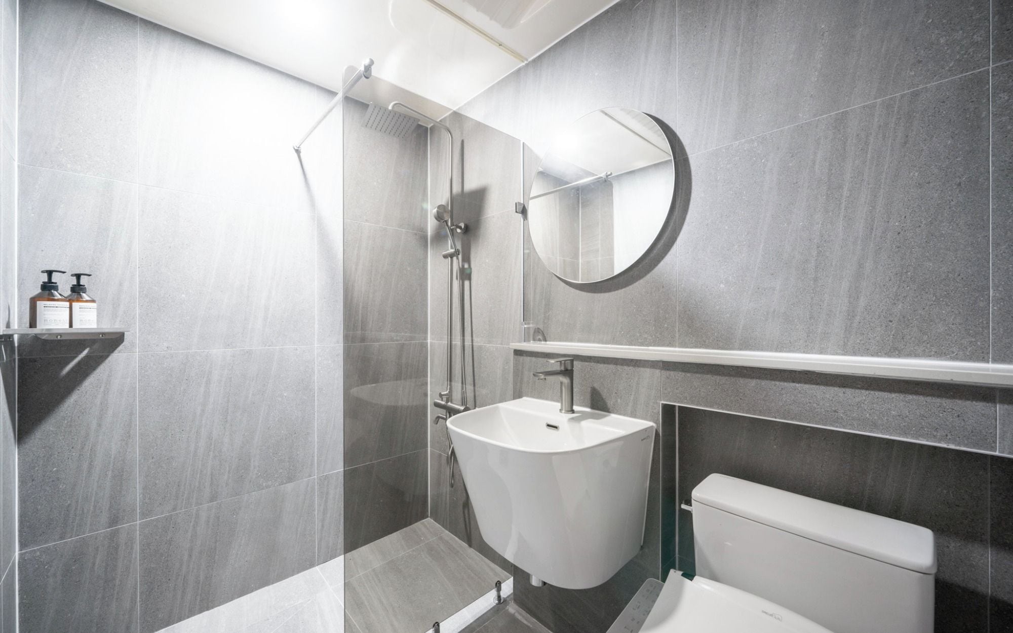 Un baño moderno con ducha envuelta en vidrio, un lavamanos blanco y un inodoro.