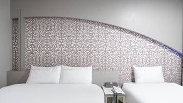 Habitación de hotel con dos camas, una pared curva con papel tapiz estampado y una mesita de noche con un teléfono.