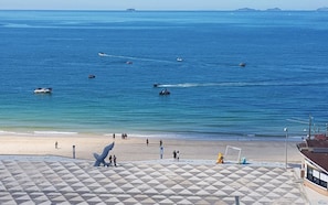 A beach with boats on the water, people on the sand, and a geometric pattern on the ground. - Bon Gaya Hotel (Boryeong)