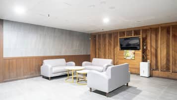 Un área de espera moderna con una televisión de pantalla plana montada en una pared de madera, dos sofás blancos, una pequeña mesa redonda y un radiador blanco.