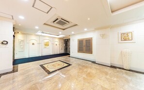 A spacious lobby with a marble floor, a central art piece, and a large wooden door. - Bon Gaya Hotel (Boryeong)