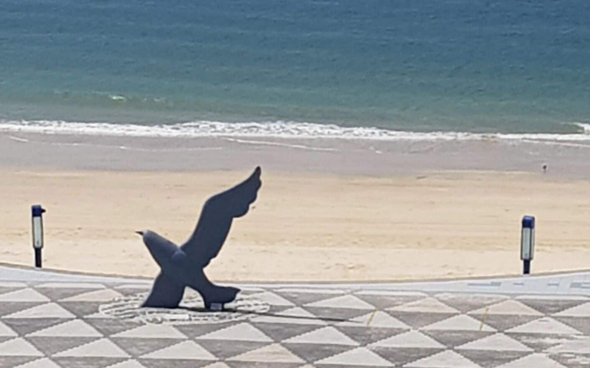 Una playa con un paseo de baldosas y una escultura de un ave.