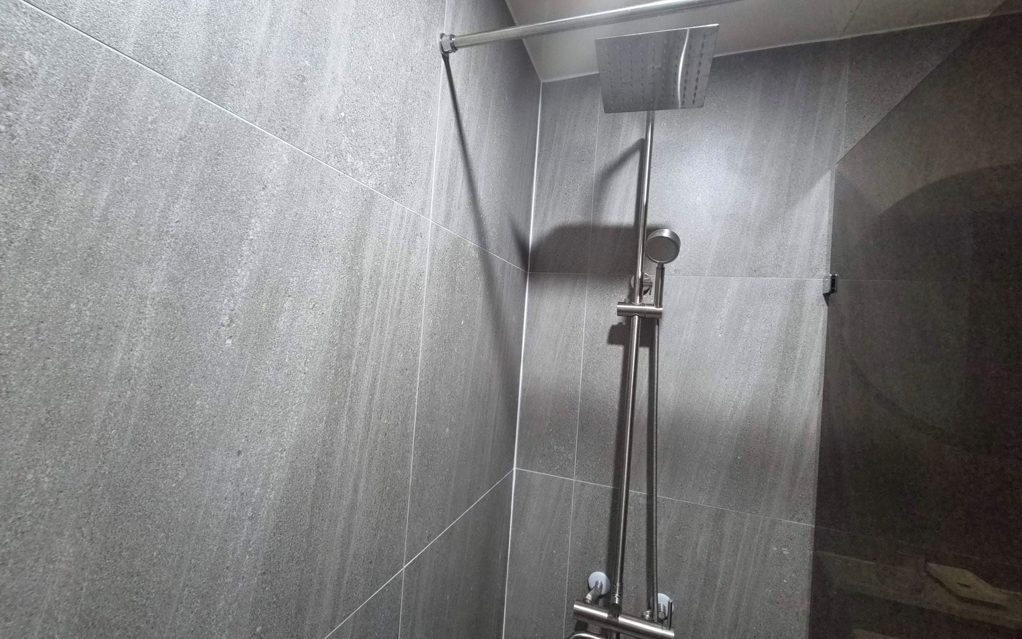 A shower with a handheld showerhead and a wall-mounted control panel.