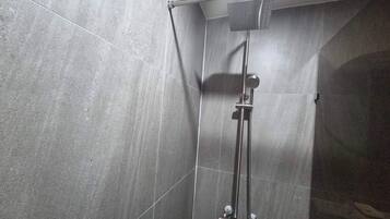 A shower with a handheld showerhead and a wall-mounted control panel.