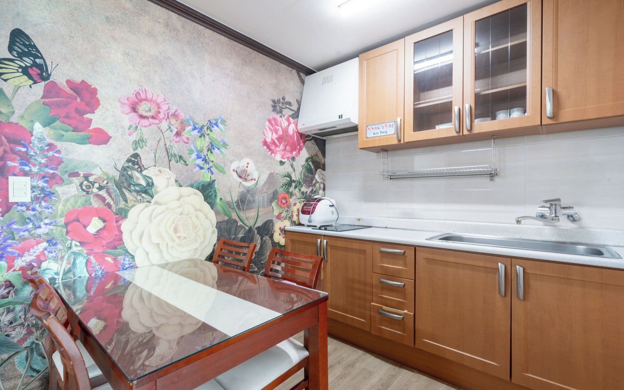Cozinha com armários de madeira, bancada branca e um mural floral na parede.