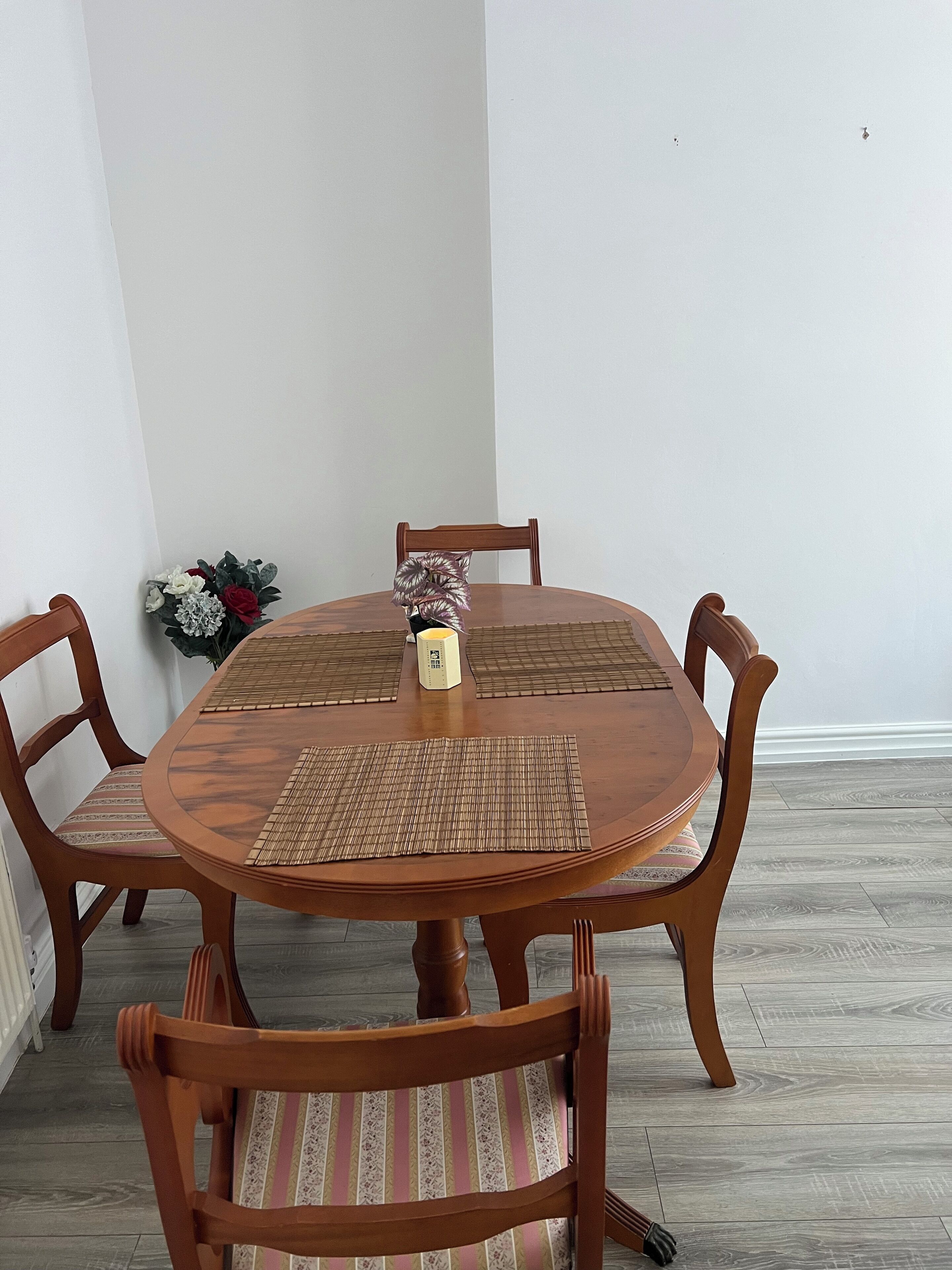 Une table de salle à manger ronde en bois, accompagn ée de quatre chaises, chacune dotée d’un siège rembourré. Un set de table est placé au centre de la table.