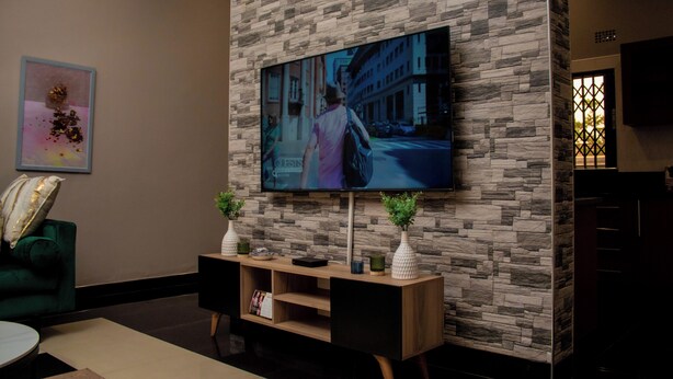 Ein modernes Wohnzimmer mit einer Wand im Steinoptik, einem flachbildfernseher, der über einer Holzkonsole angebracht ist, und einem grünen Sofa.