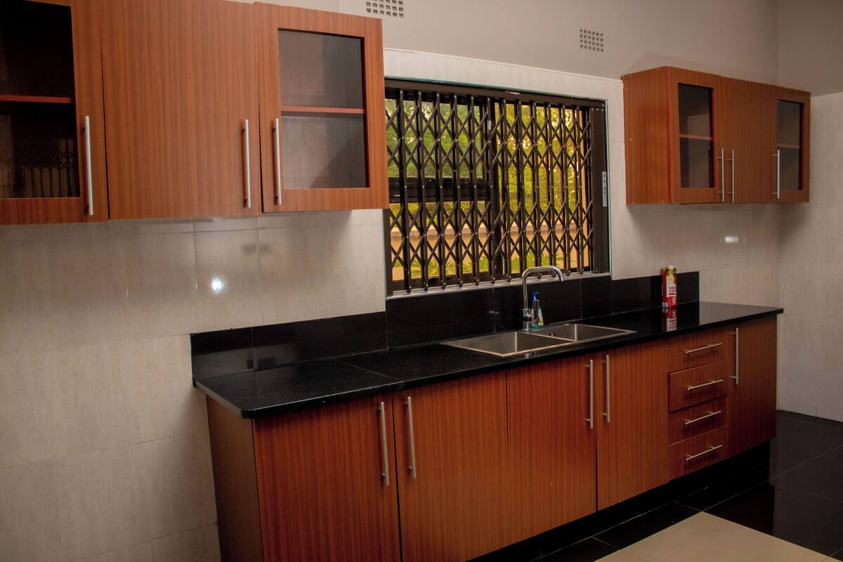 A kitchen with wooden cabinets, a black countertop, and a window with a metal security screen.