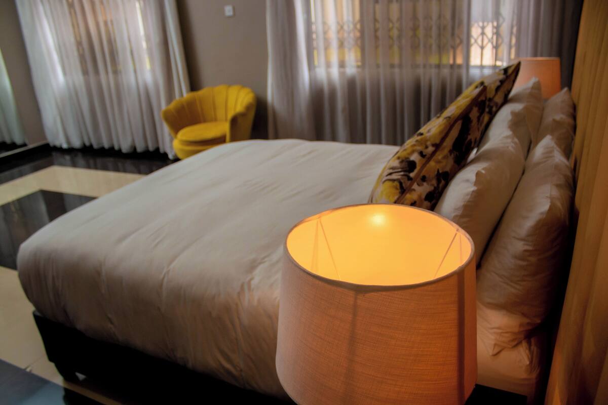 A hotel room with a large bed, a yellow armchair, and a lamp.