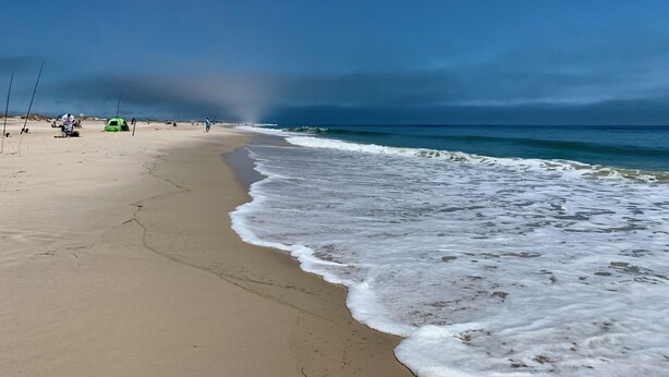 Een strand met een zandstrand, enkele visstokken en een tent.