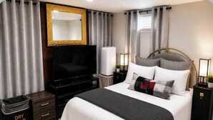 Ein Hotelzimmer mit einem Bett, einem Fernseher, einem Nachttisch, einer Lampe, einem Spiegel und einem Fenster mit Vorhängen.