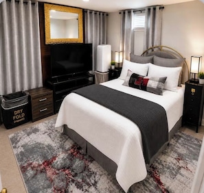 Une chambre d’hôtel avec un lit, une télévision, une table de chevet, une lampe, un miroir et une fenêtre avec des rideaux.