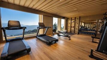 Un gimnasio espacioso con cintas de correr, una máquina de remo y equipo de levantamiento de pesas. Amplias ventanas ofrecen vistas al exterior.
