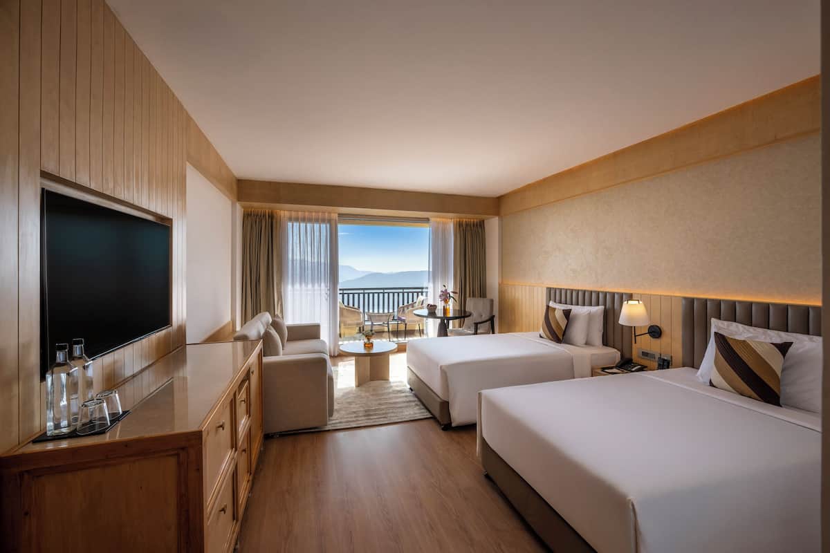 A hotel room with a large flat-screen TV, two beds, a sofa, a dining table, and a balcony with a view.