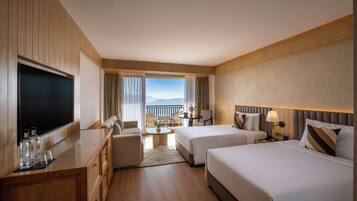 A hotel room with a large flat-screen TV, two beds, a sofa, a dining table, and a balcony with a view.