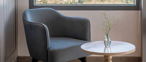 A room with a large window offering a mountain view, a grey armchair, and a small round table with a vase.