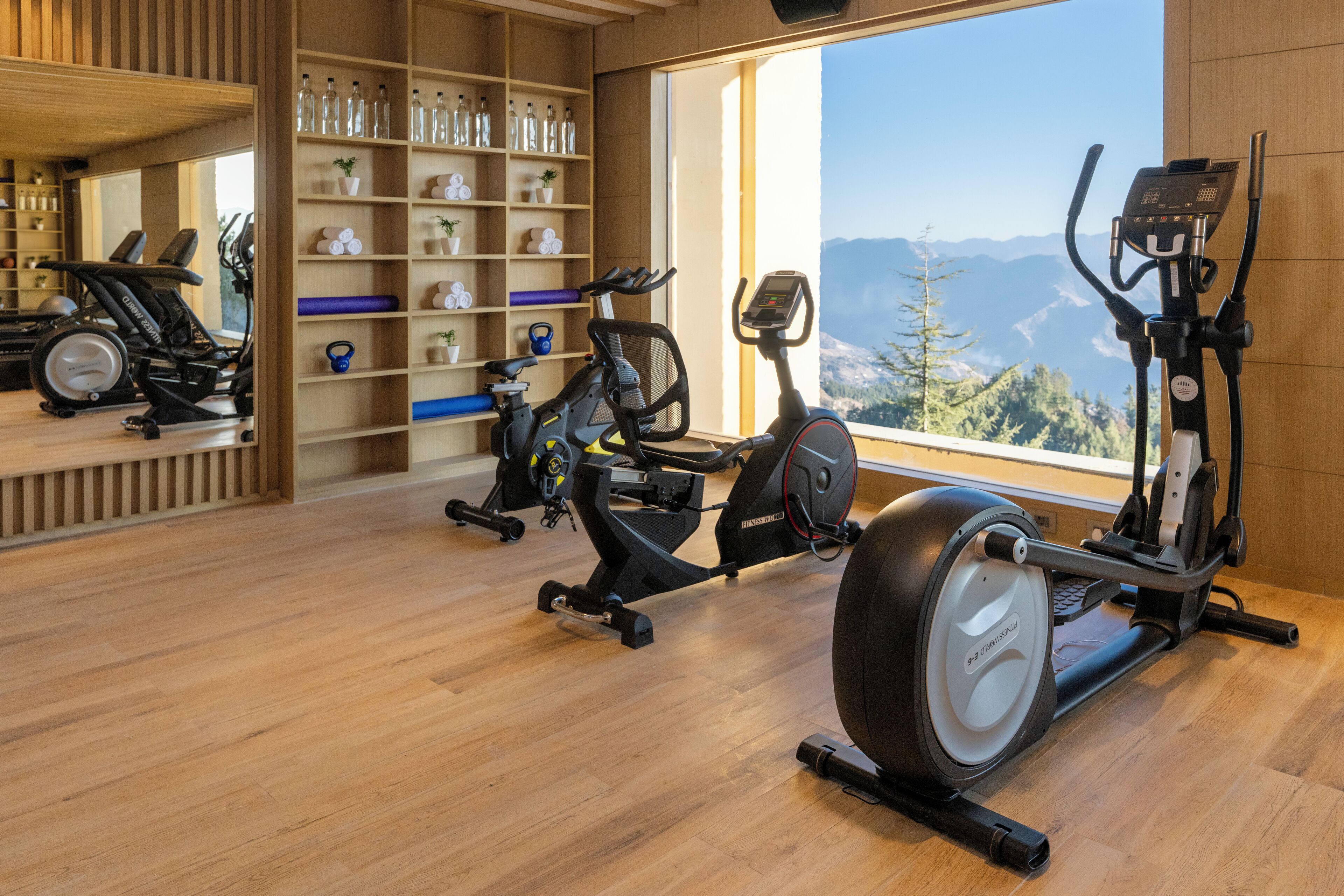 A gym with exercise equipment, a wooden floor, and a large window with a mountain view.
