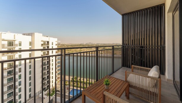 Ein Balkon mit einem Holztisch und zwei Korbstühlen, mit Blick auf ein Gewässer und angrenzende Gebäude.