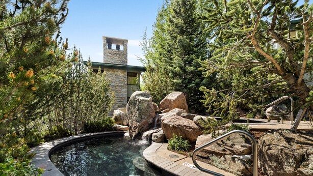 A hot tub surrounded by rocks and trees, with a stone building in the background. - Tamarack Townhome #17 (Snowmass Village)