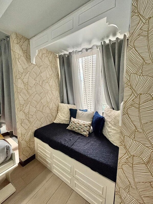 Una habitación acogedora con cama, cortinas y un papel tapiz estampado.