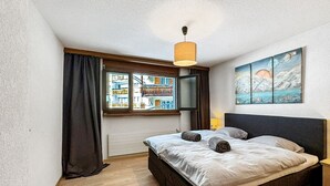 Une chambre à coucher avec un lit, une fenêtre avec des rideaux, un tableau au mur et un luminaire suspendu.