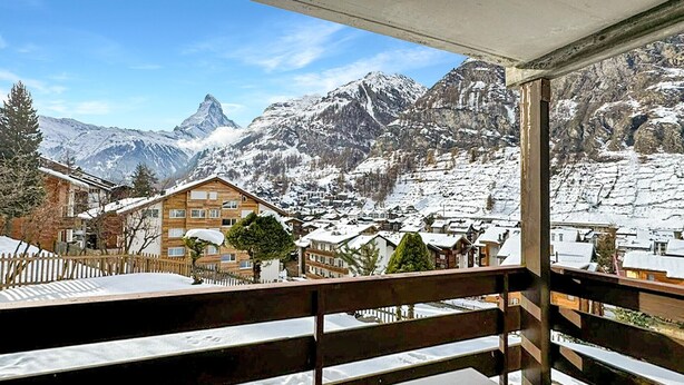 Un balcon offrant une vue sur des montagnes enneigées et un bâtiment de style chalet.