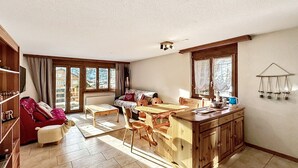 Un vaste espace de vie comprenant une table à manger en bois, un canapé et un coin cuisine avec des meubles en bois et une fenêtre.