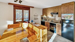 Une cuisine dotée de meubles en bois, d’un réfrigérateur en acier inoxydable et d’un coin repas avec une table et des bancs en bois.