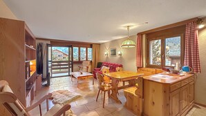 Une cuisine chaleureuse, avec des meubles en bois, une table à manger et une vue sur un paysage montagneux par les fenêtres.