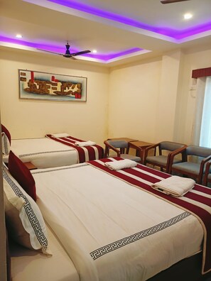 A hotel room with two beds, a ceiling fan, a painting, a table, and four chairs. - Ariees Grand (Port Blair)