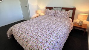 A neatly made bed with a floral bedspread, a bedside table with a lamp, and a door to the left. - Socialisers Dream on Arawa!  (Ohakune)
