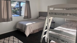 A bedroom with a bunk bed, a single bed, a window with curtains, and a small bedside table. - Socialisers Dream on Arawa!  (Ohakune)