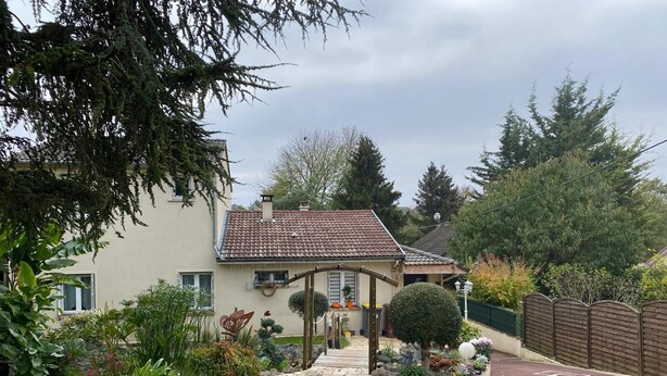 A house with a tiled roof, a stone pathway leading to the entrance, and a variety of plants and shrubs in the garden. - One-bedroom apartment near Disney and Paris (Dampmart)