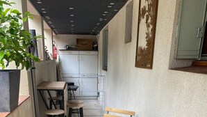 A small, enclosed patio area with a round table and wooden chairs, a potted plant, and a metal shelf with items on it. - One-bedroom apartment near Disney and Paris (Dampmart)
